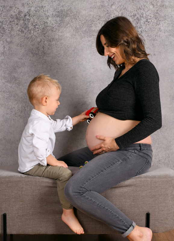 Schwangere Mama sitz mit Geschwisterkind auf Bank